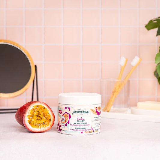 Visuel du pot Masque sorbet Tendre Passion posé sur un plan de salle de bain rose, à côté d'un fruit de la passion coupé en deux