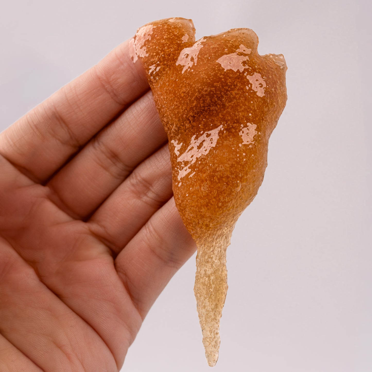 Visuel de la texture granuleuse du Gommage Capillaire au Sucre de Canne Actidetox tenu entre les doigts sur fond clair