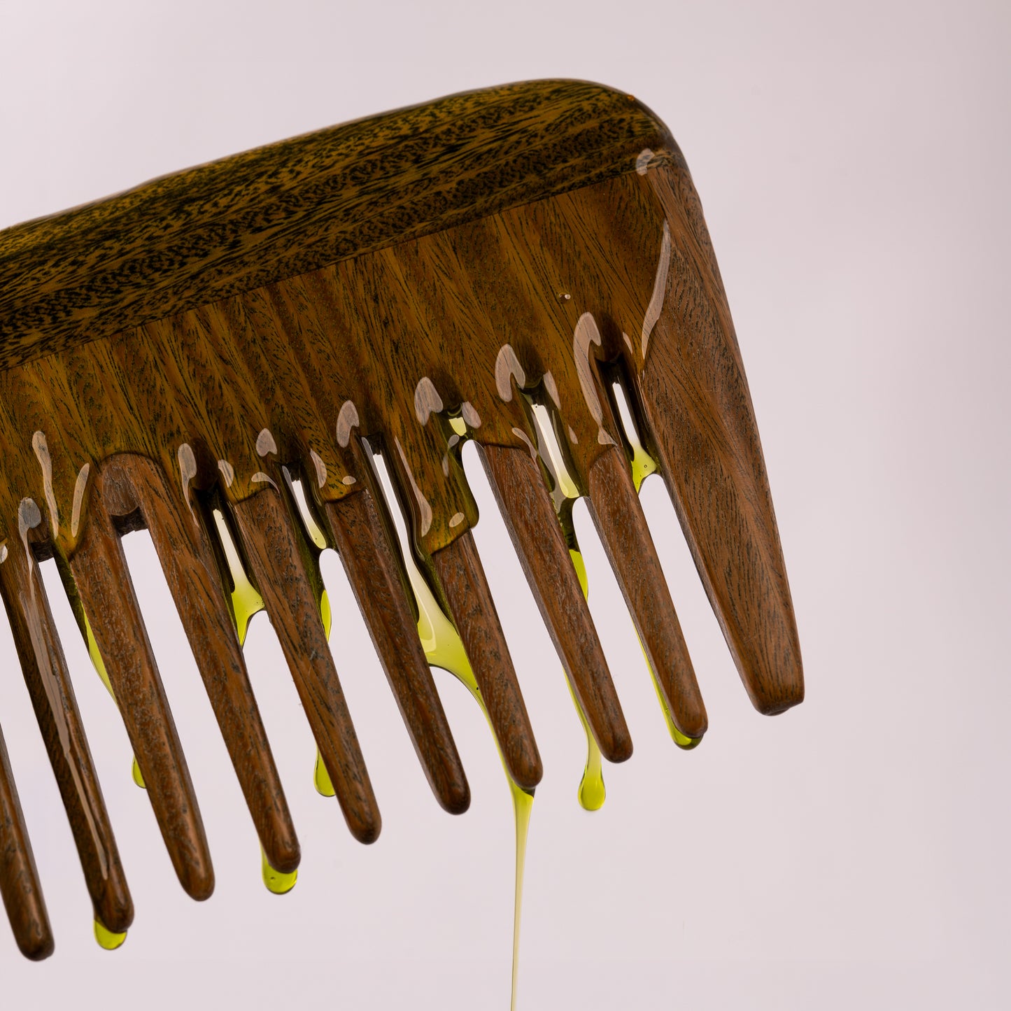 Visuel de la texture huileuse verte du Sérum Riche Actigro s'écoulant le long d'un peigne en bois sur fond clair