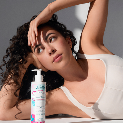 Femme aux cheveux bouclés allongée, posant derrière le lait thermo-protecteur Acticurl Expert