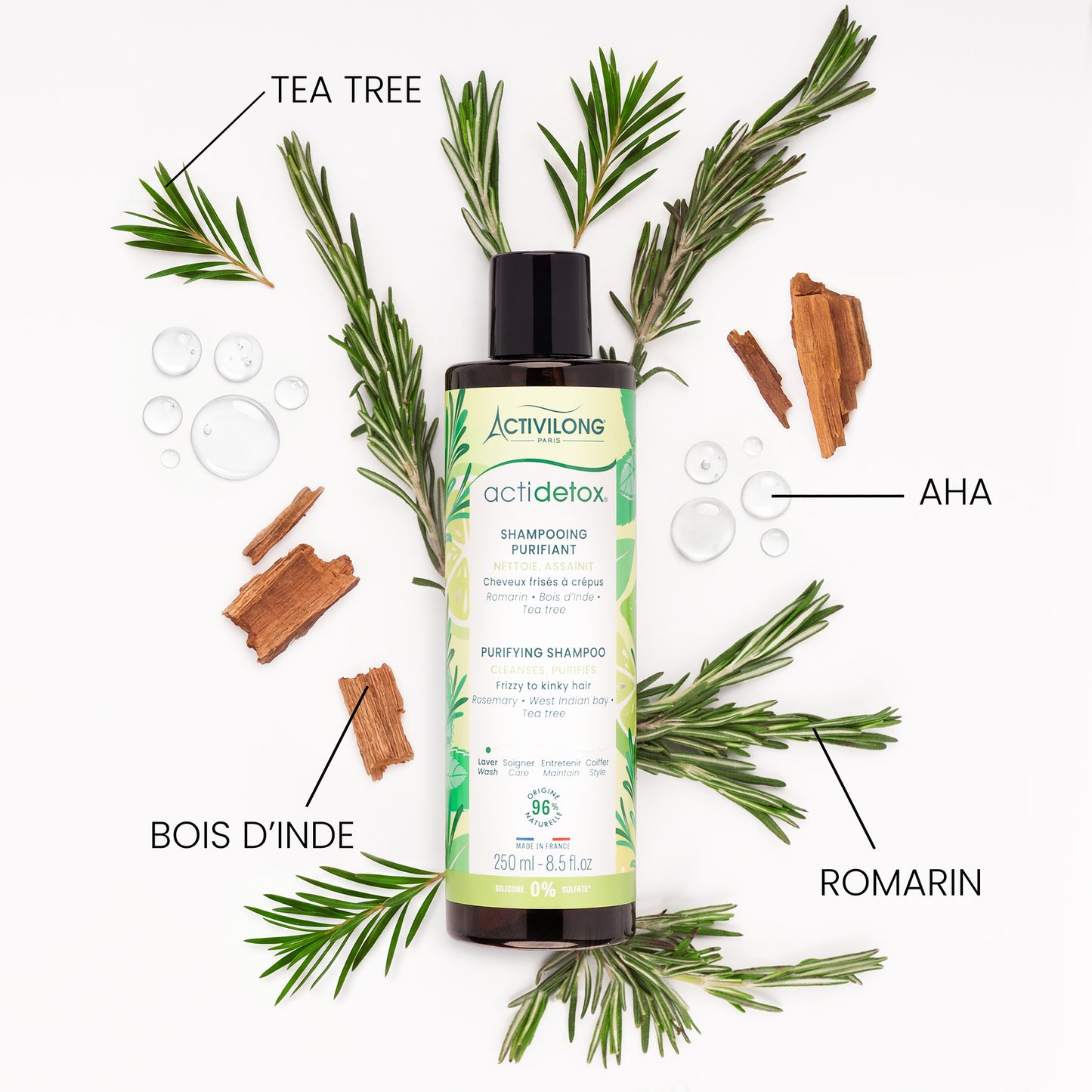 Flacon de Shampooing purifiant Actidetox entouré de ses actifs sur fond blanc : branches de romarin, rameaux de tea tree, morceaux d'écorce de bois d'Inde et gouttes d'AHA, avec les mentions « Tea tree », « Romarin », « Bois d'Inde » et « AHA ».