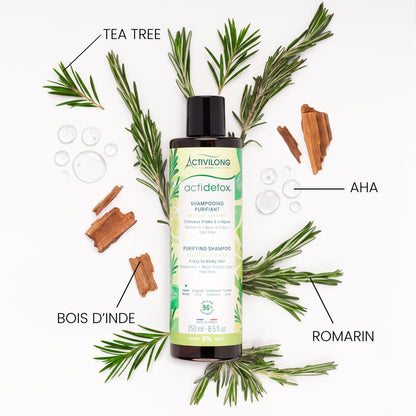 Flacon de Shampooing purifiant Actidetox entouré de ses actifs sur fond blanc : branches de romarin, rameaux de tea tree, morceaux d'écorce de bois d'Inde et gouttes d'AHA, avec les mentions « Tea tree », « Romarin », « Bois d'Inde » et « AHA ».