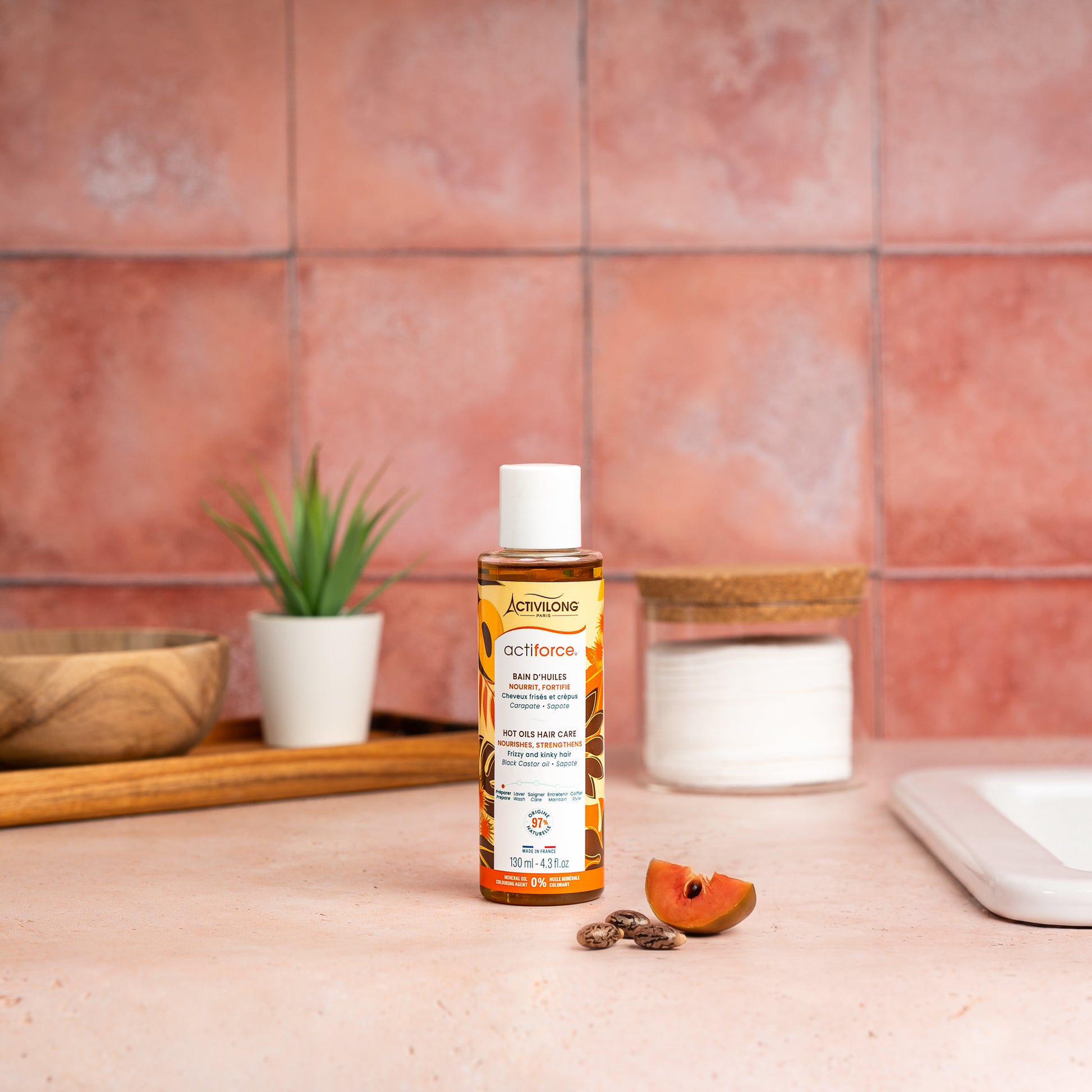 Visuel d'un Flacon du Bain d'Huiles Actiforce sur un plan de salle de bain terracotta, avec graines de carapate et tranche de sapote en arrière plan