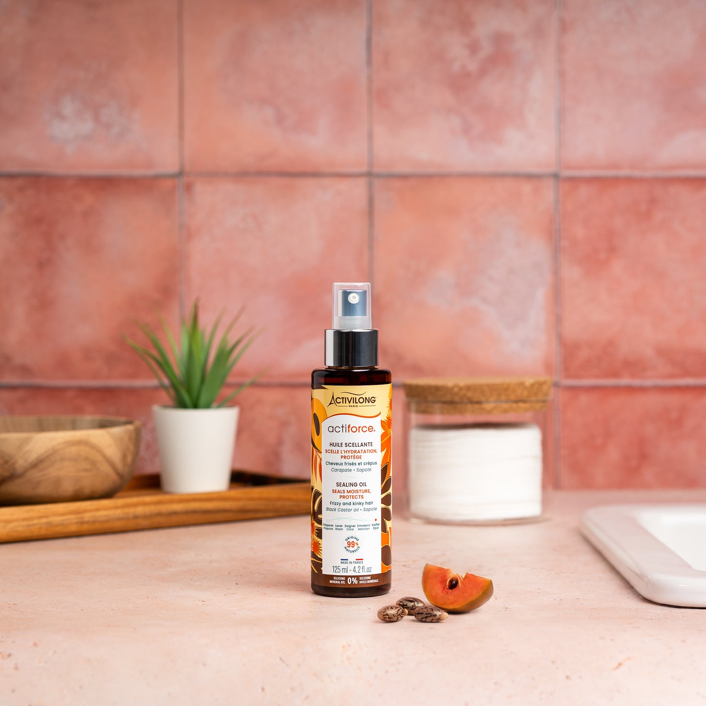 Visuel d'un Flacon de l'Huile Scellante Actiforce sur un plan de salle de bain terracotta, avec graines de carapate et tranche de sapote en arrière plan