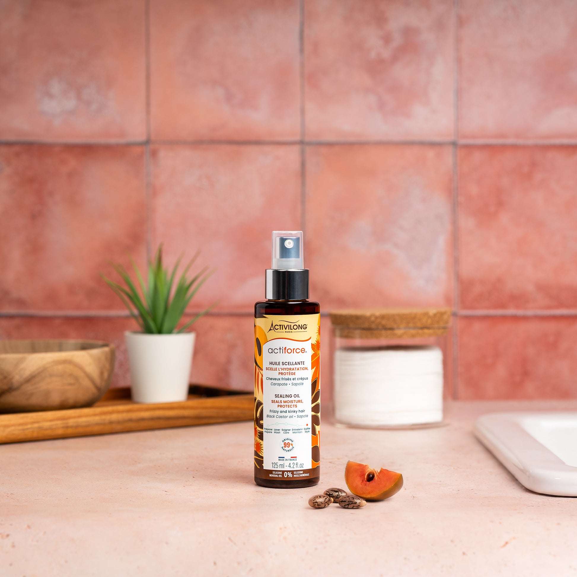 Visuel d'un Flacon de l'Huile Scellante Actiforce sur un plan de salle de bain terracotta, avec graines de carapate et tranche de sapote en arrière plan