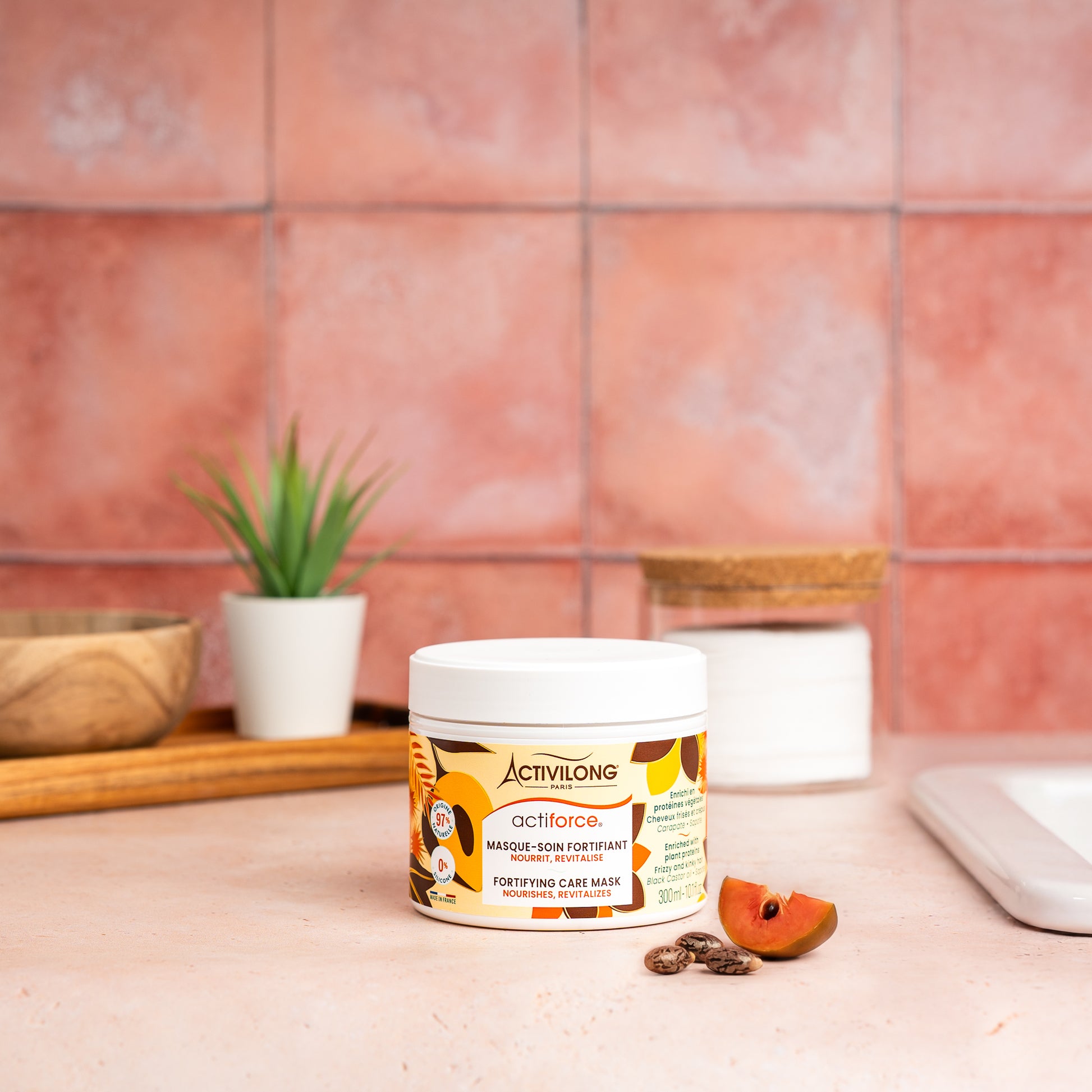 Visuel d'un Pot du Masque-Soin Fortifiant Actiforce sur un plan de salle de bain terracotta, avec graines de carapate et tranche de sapote en arrière plan