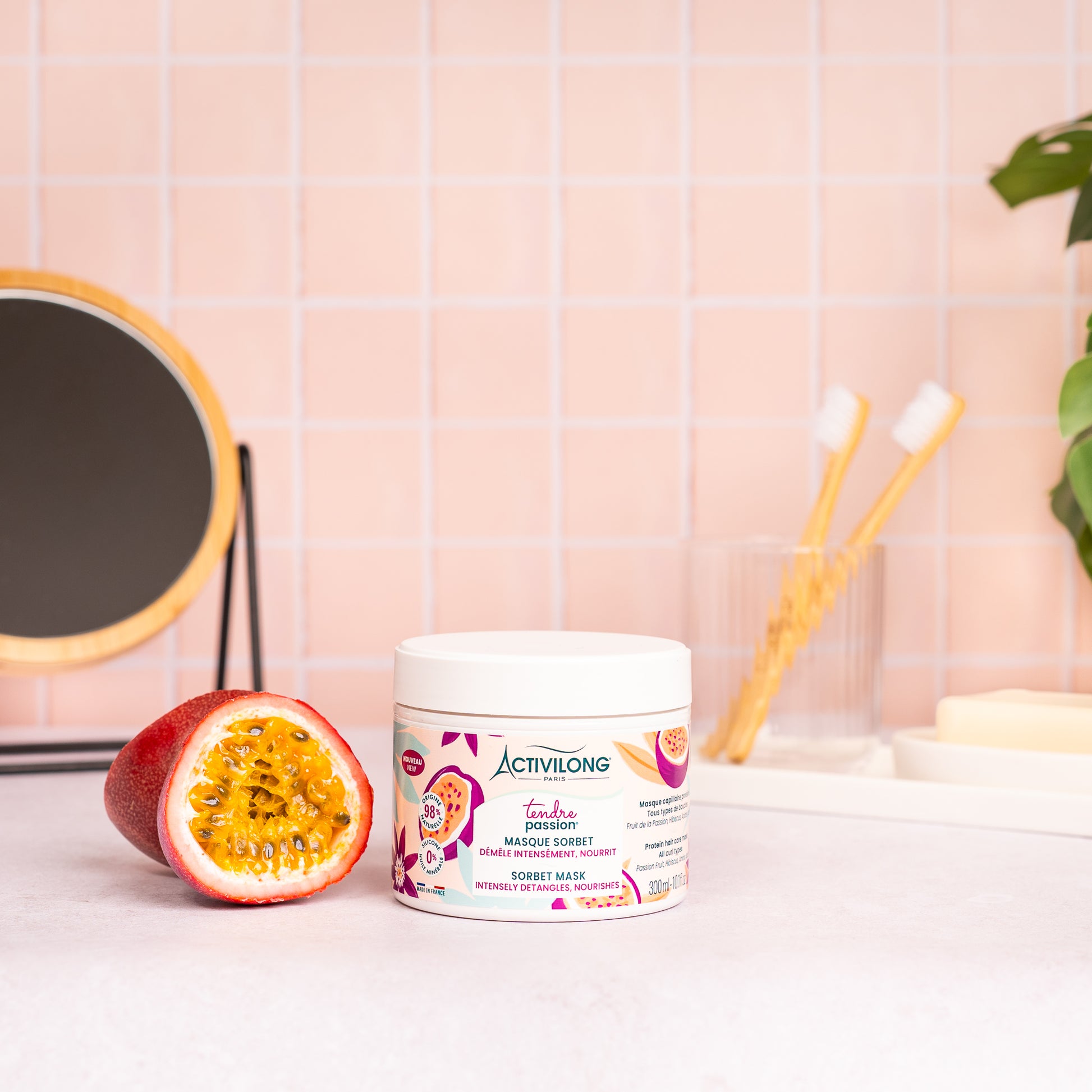 Visuel du pot Masque sorbet Tendre Passion posé sur un plan de salle de bain rose, à côté d'un fruit de la passion coupé en deux