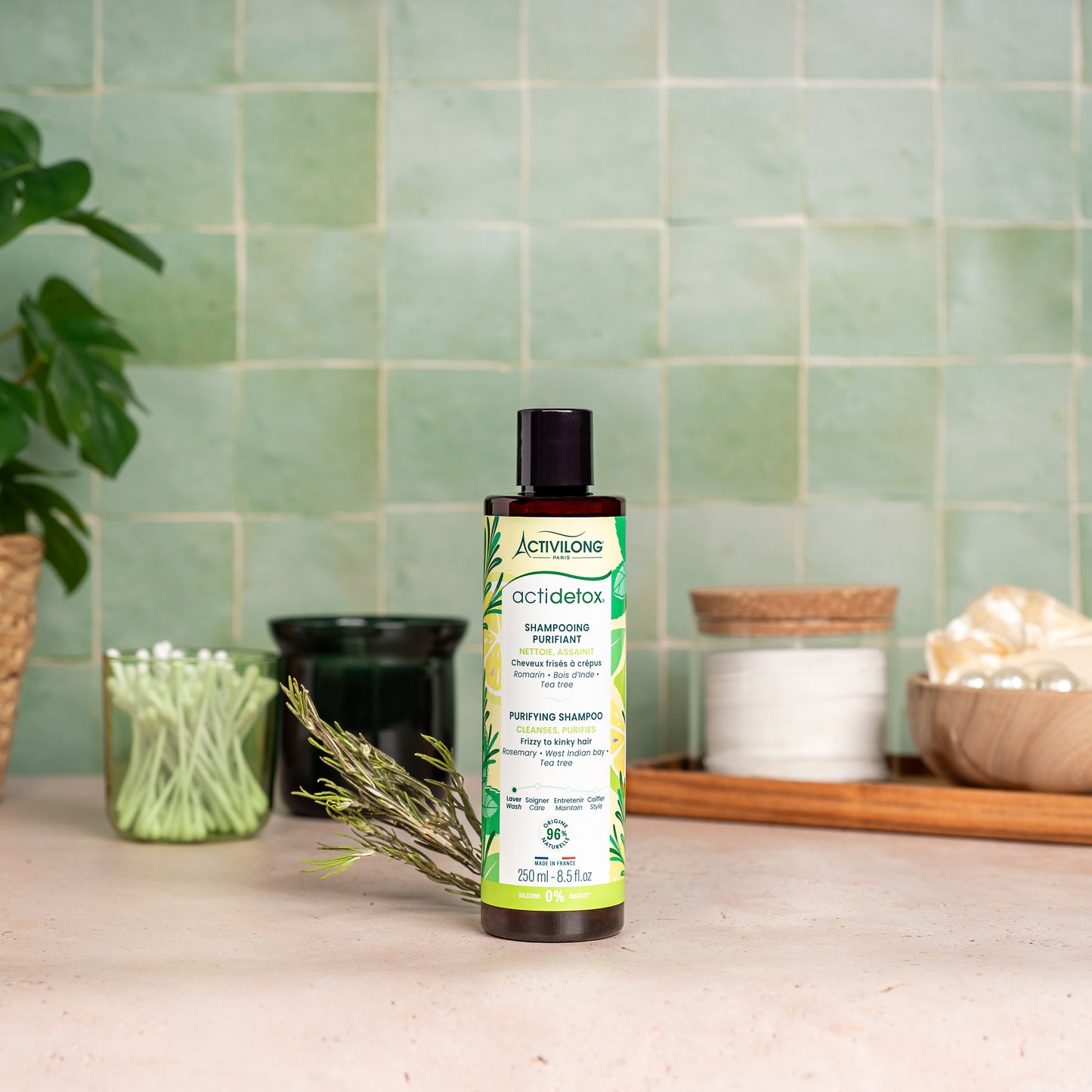 Visuel d'un Flacon du Shampooing Purifiant Actidetox sur un plan de salle de bain vert, avec brin de romarin et accessoires en arrière plan
