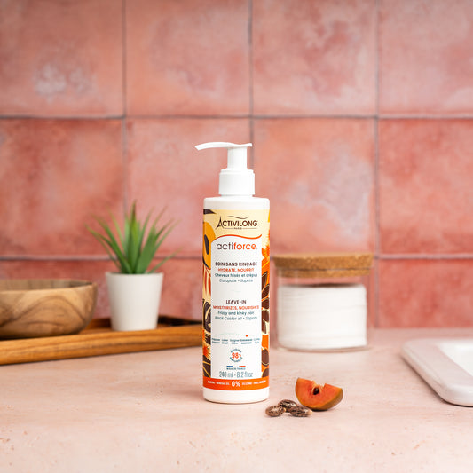 Visuel d'un Flacon de 240 ml du Soin Sans Rinçage Actiforce sur un plan de salle de bain terracotta, avec graines de carapate et tranche de sapote en arrière plan