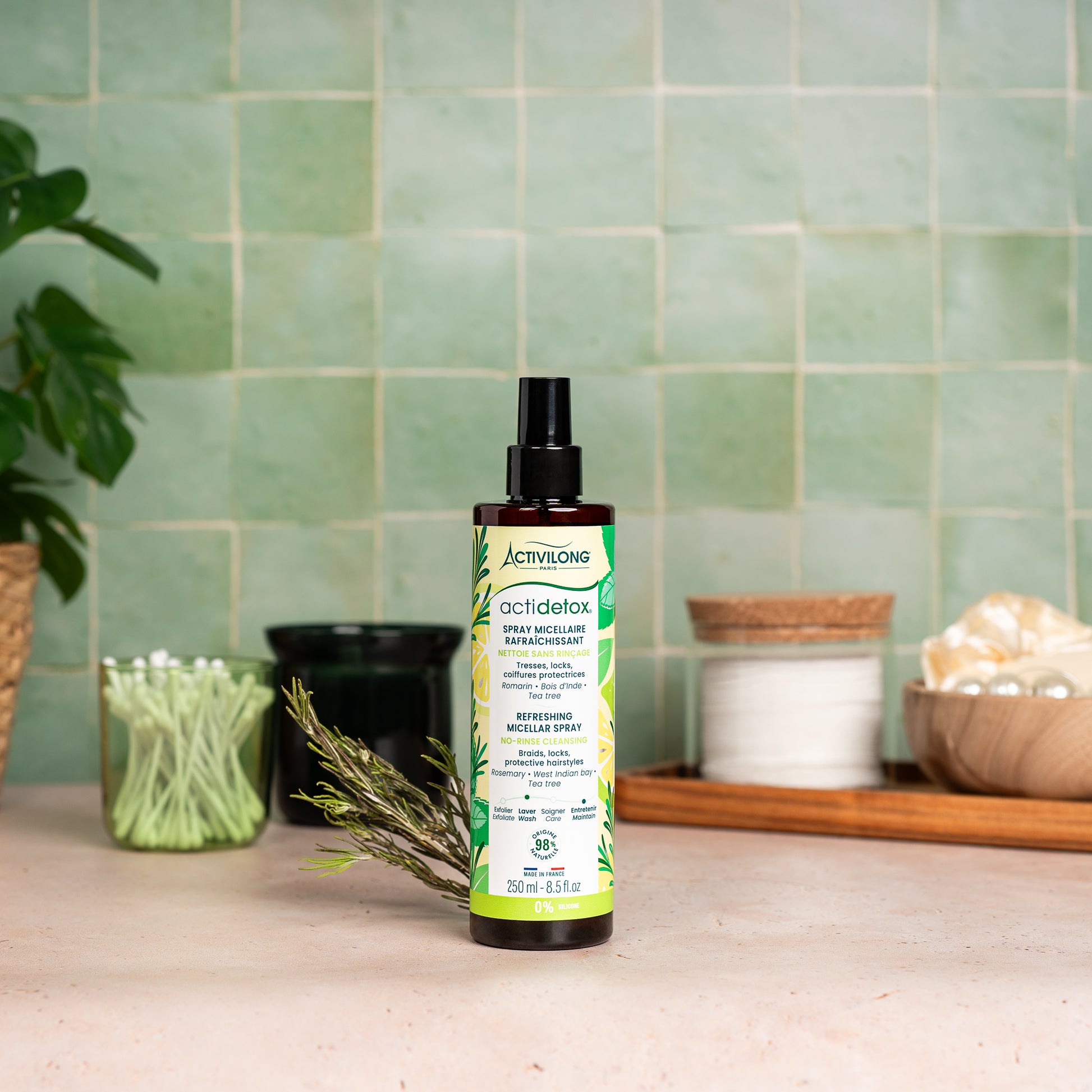 Visuel d'un Flacon du Spray Micellaire Rafraîchissant Actidetox sur un plan de salle de bain vert, avec brin de romarin et accessoires en arrière plan