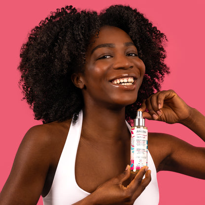 Visuel d'une femme aux cheveux crépus volumineux, souriante, tenant le flacon Sérum définissant Acticurl Activilong, sur fond rose vif