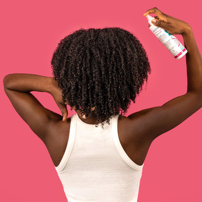 Visuel d'une femme vue de dos aux cheveux crépus volumineux vaporisant le Spray activateur de boucles Acticurl Activilong sur sa chevelure, sur fond rose vif