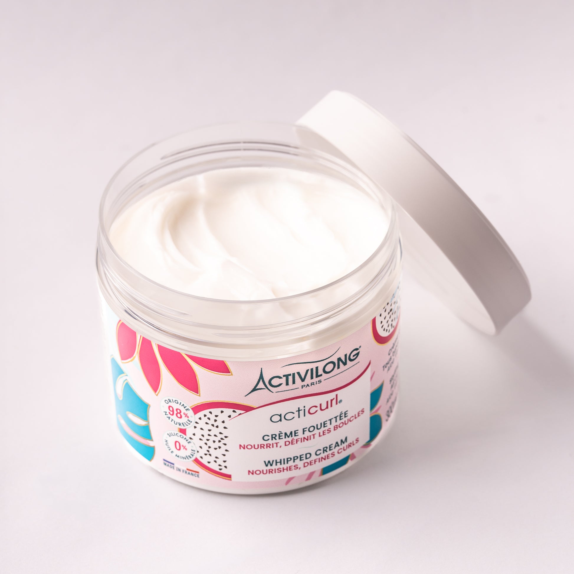 Visuel d’un Pot de la Crème Fouettée Acticurl ouvert sur fond rose pâle, avec texture crème visible et couvercle en arrière plan
