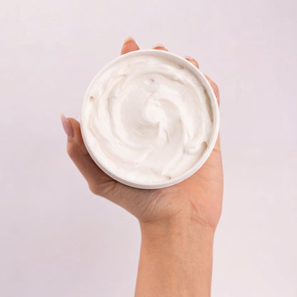 Pot ouvert de Crème sorbet Coco d'Amour tenu en main, vu de dessus, révélant sa texture sorbet blanche fouettée et tourbillonnée, sur fond gris clair rosé.