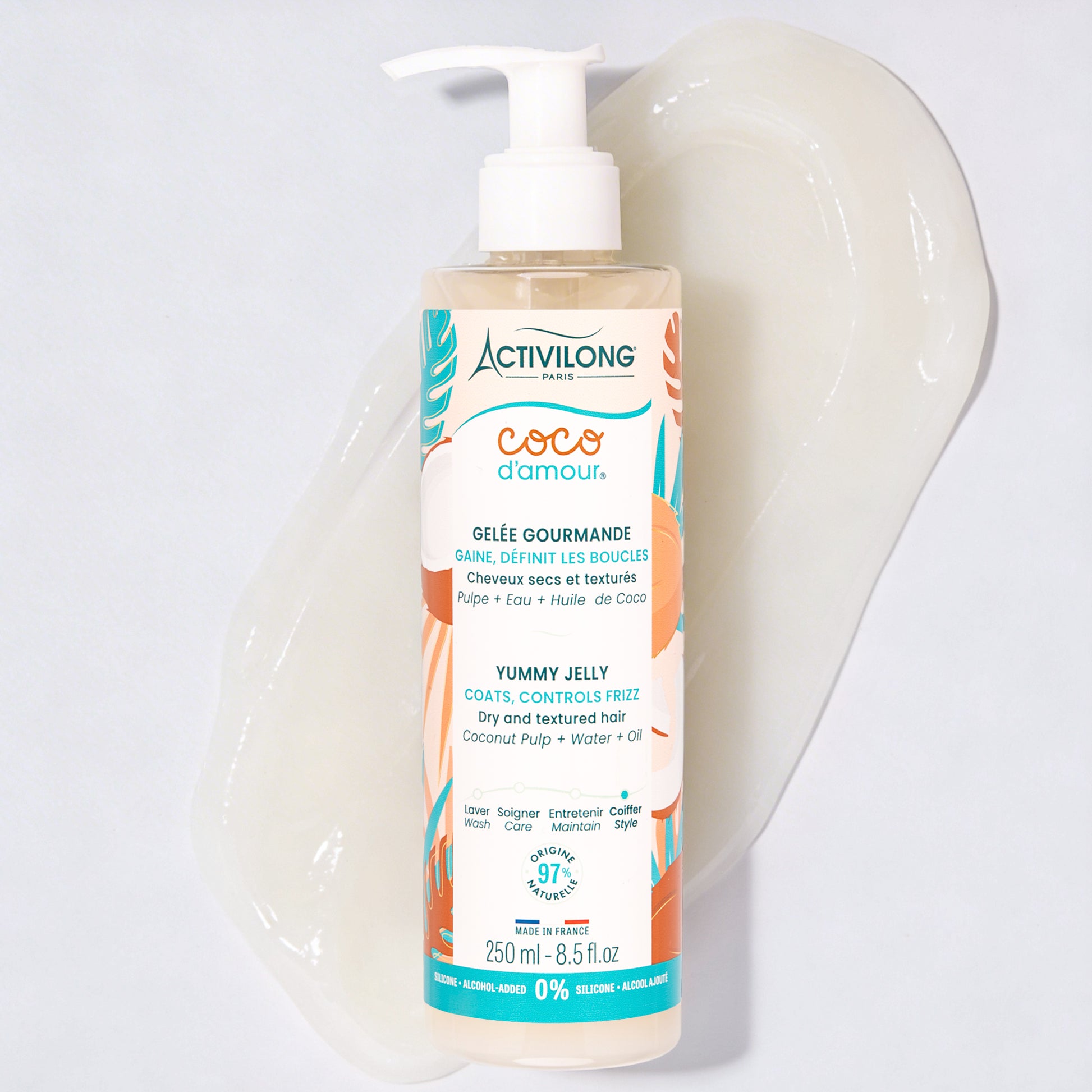 Flacon-pompe de Gelée gourmande Coco d'Amour posé sur une large trace de produit étalée, révélant sa texture de gelée translucide et brillante, sur fond gris clair.