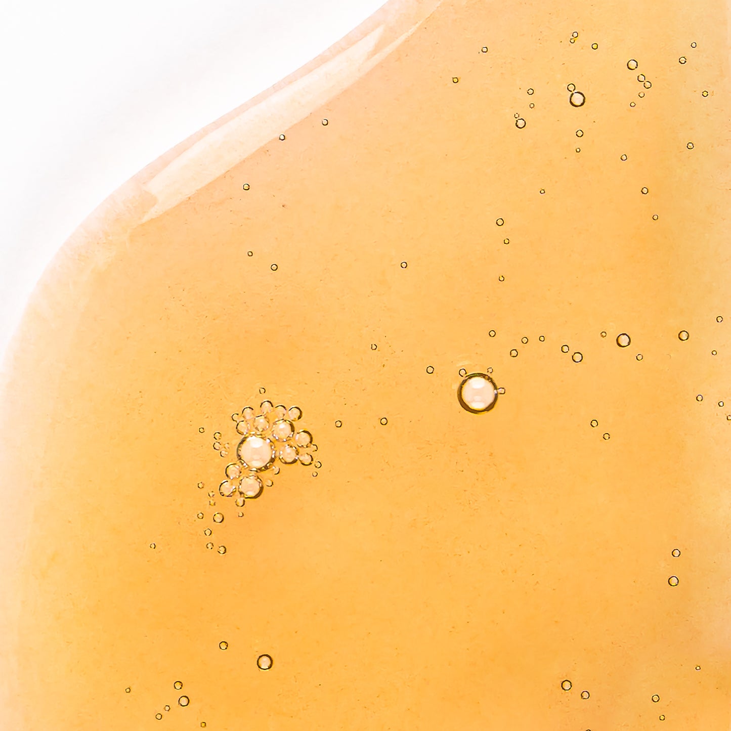 Visuel de la texture huileuse dorée de l'Huile Scellante Actiforce parsemée de bulles sur fond clair