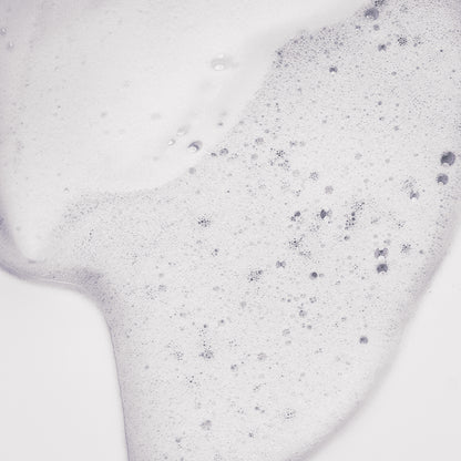 Texture de la Mousse de maracuja Tendre Passion étalée en gros plan, mousse blanche aérée et mousseuse aux fines bulles, sur fond gris clair.