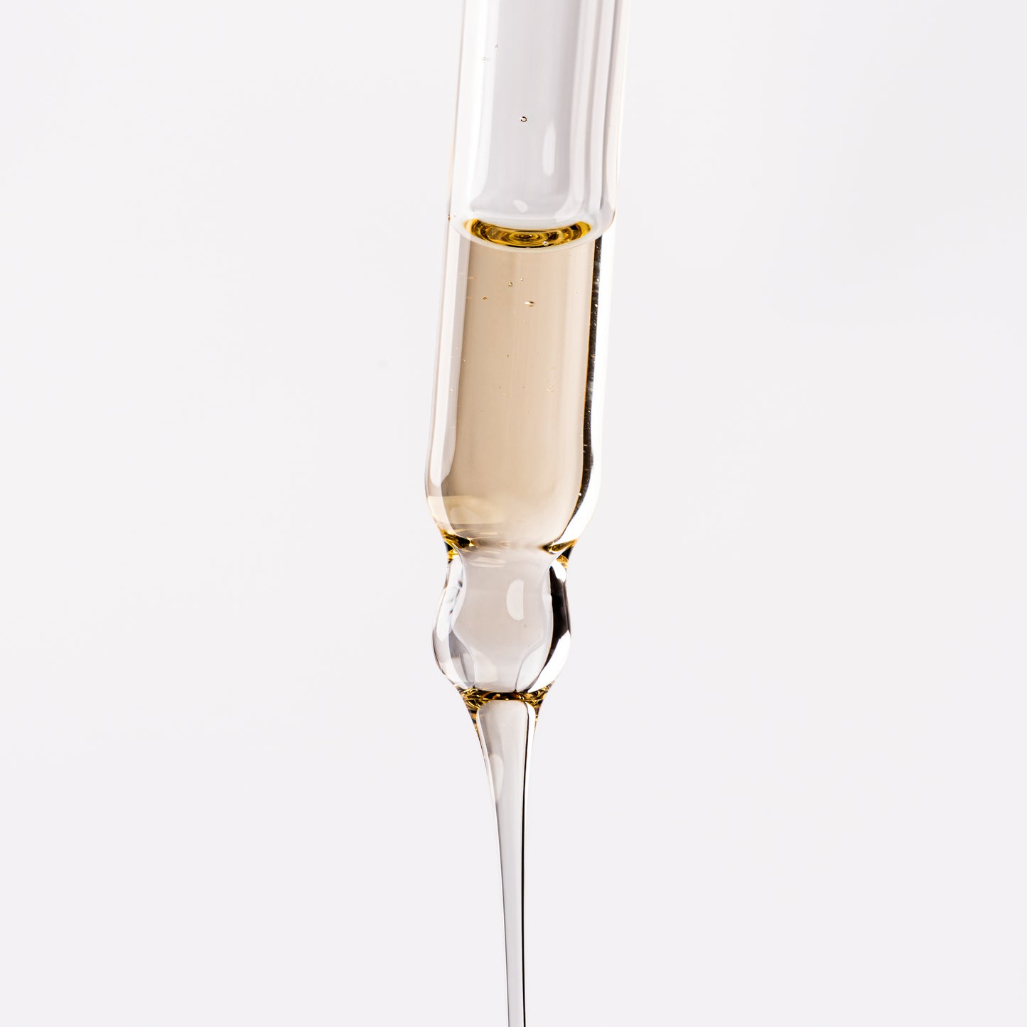 Visuel de la texture fluide dorée du Sérum Fluide Actigro s'écoulant d'une pipette compte-gouttes sur fond clair