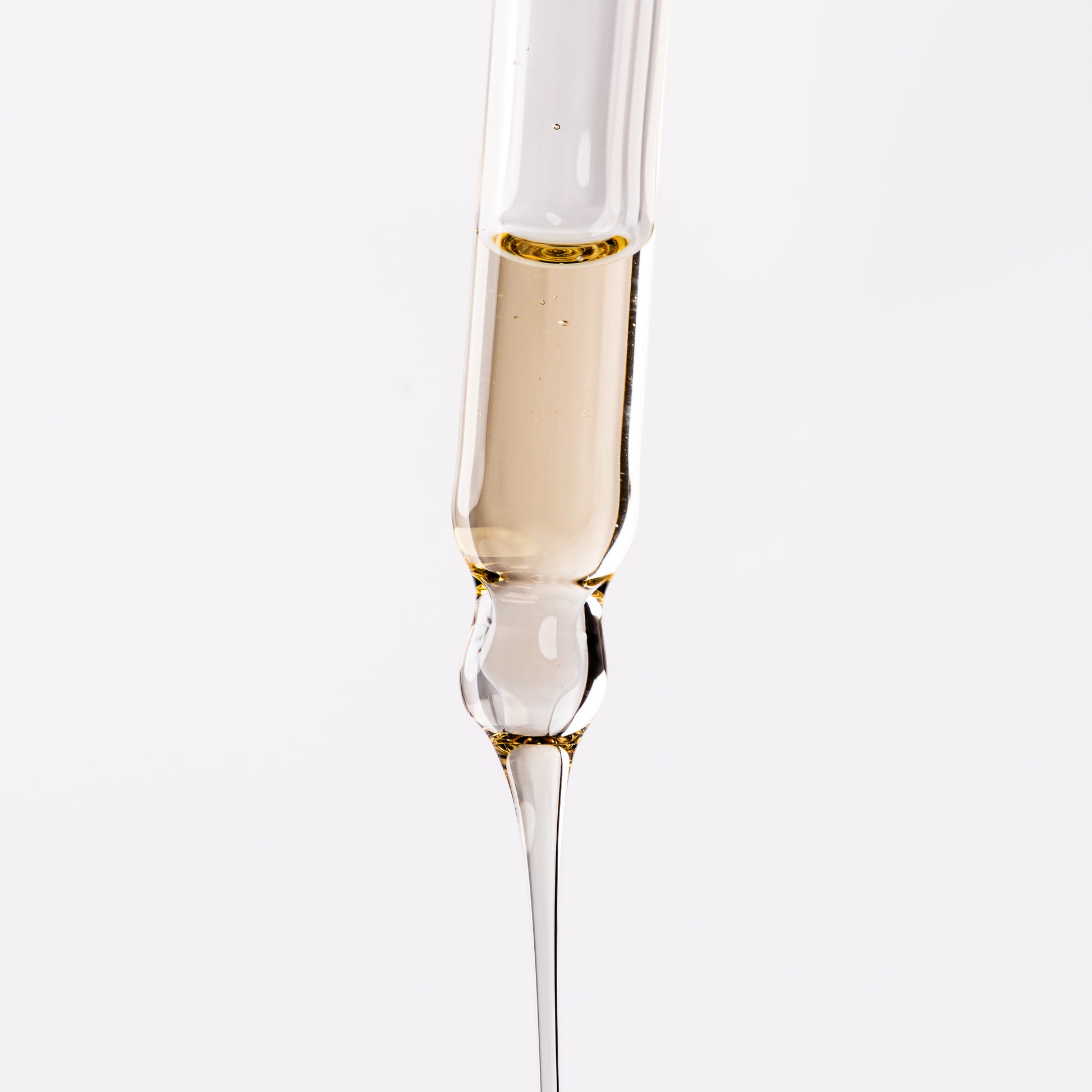 Visuel de la texture fluide dorée du Sérum Fluide Actigro s'écoulant d'une pipette compte-gouttes sur fond clair