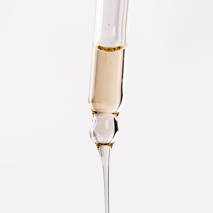 Visuel de la texture fluide dorée du Sérum Fluide Actigro s'écoulant d'une pipette compte-gouttes sur fond clair