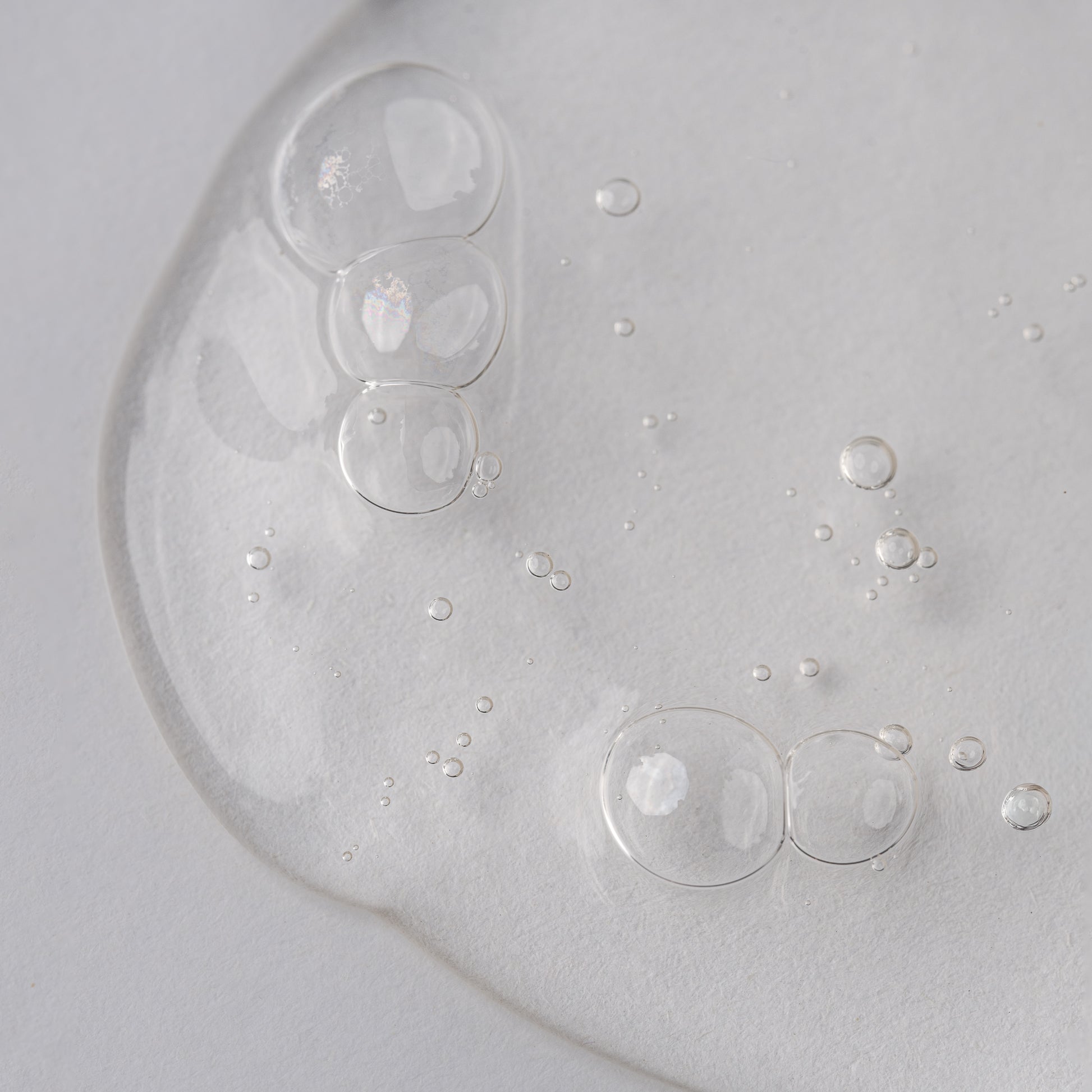 Visuel de la texture gélifiée transparente du Shampooing Purifiant Actidetox parsemée de bulles sur fond clair