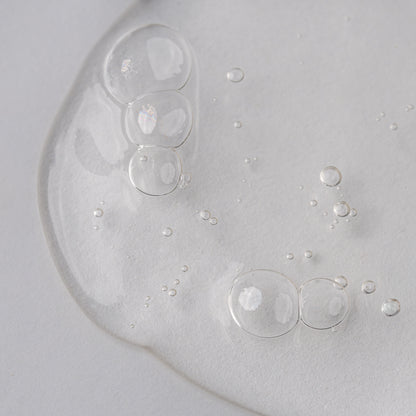 Visuel de la texture gélifiée transparente du Shampooing Purifiant Actidetox parsemée de bulles sur fond clair