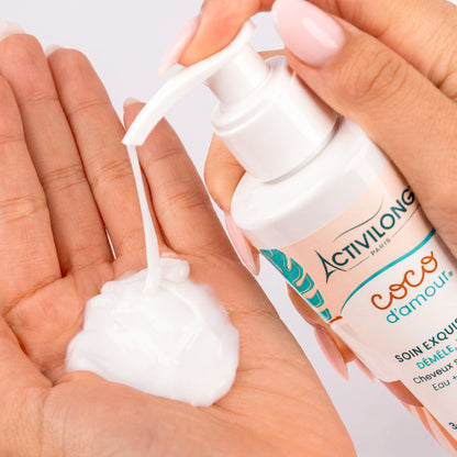Flacon-pompe de Soin exquis 3-en-1 Coco d'Amour actionné au-dessus d'une main, déposant une noisette de soin blanc à la texture lactée onctueuse, sur fond gris clair.