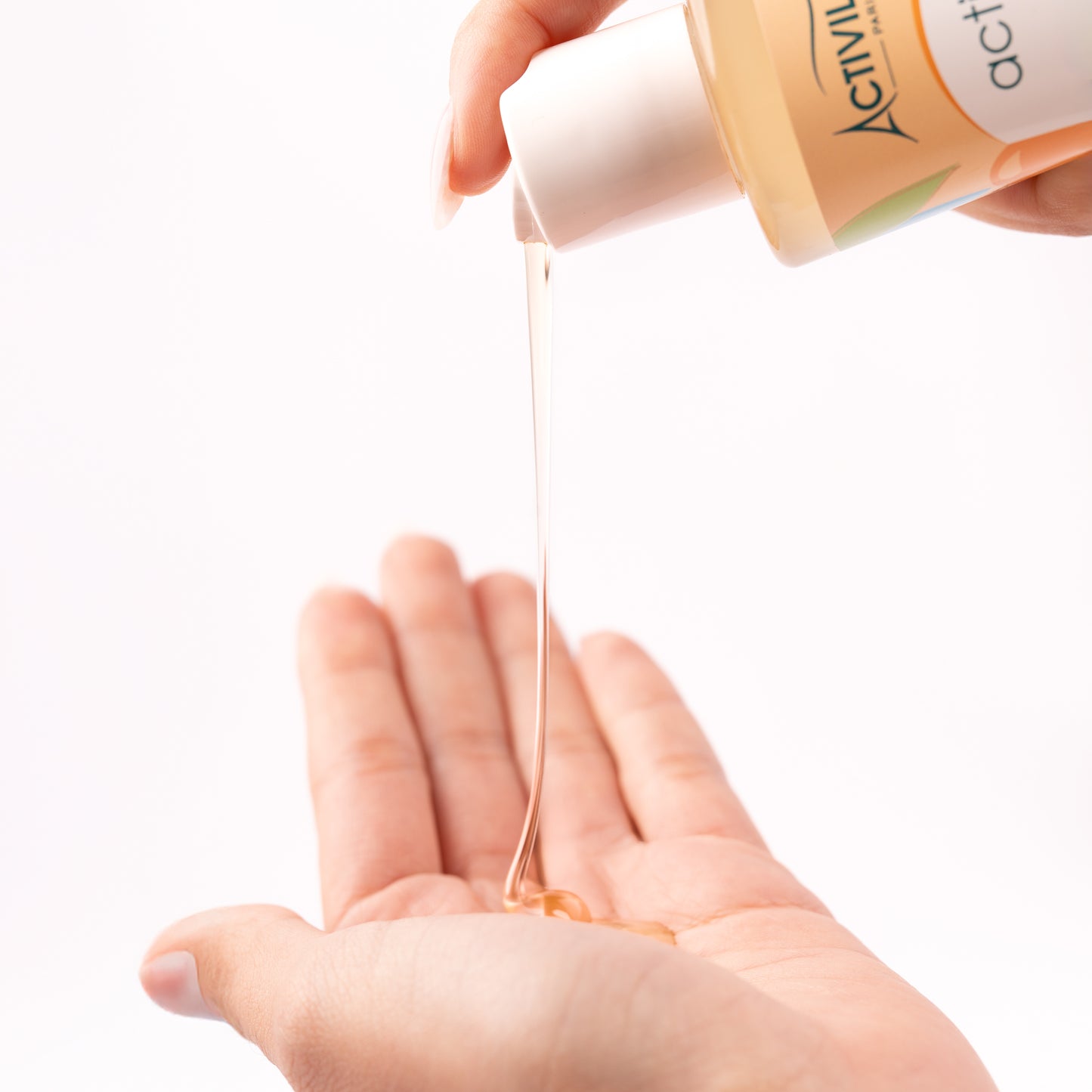 Ti Shampooing Conditionneur Actikids versé dans le creux d'une main, révélant sa texture fluide et translucide ambrée, sur fond blanc.