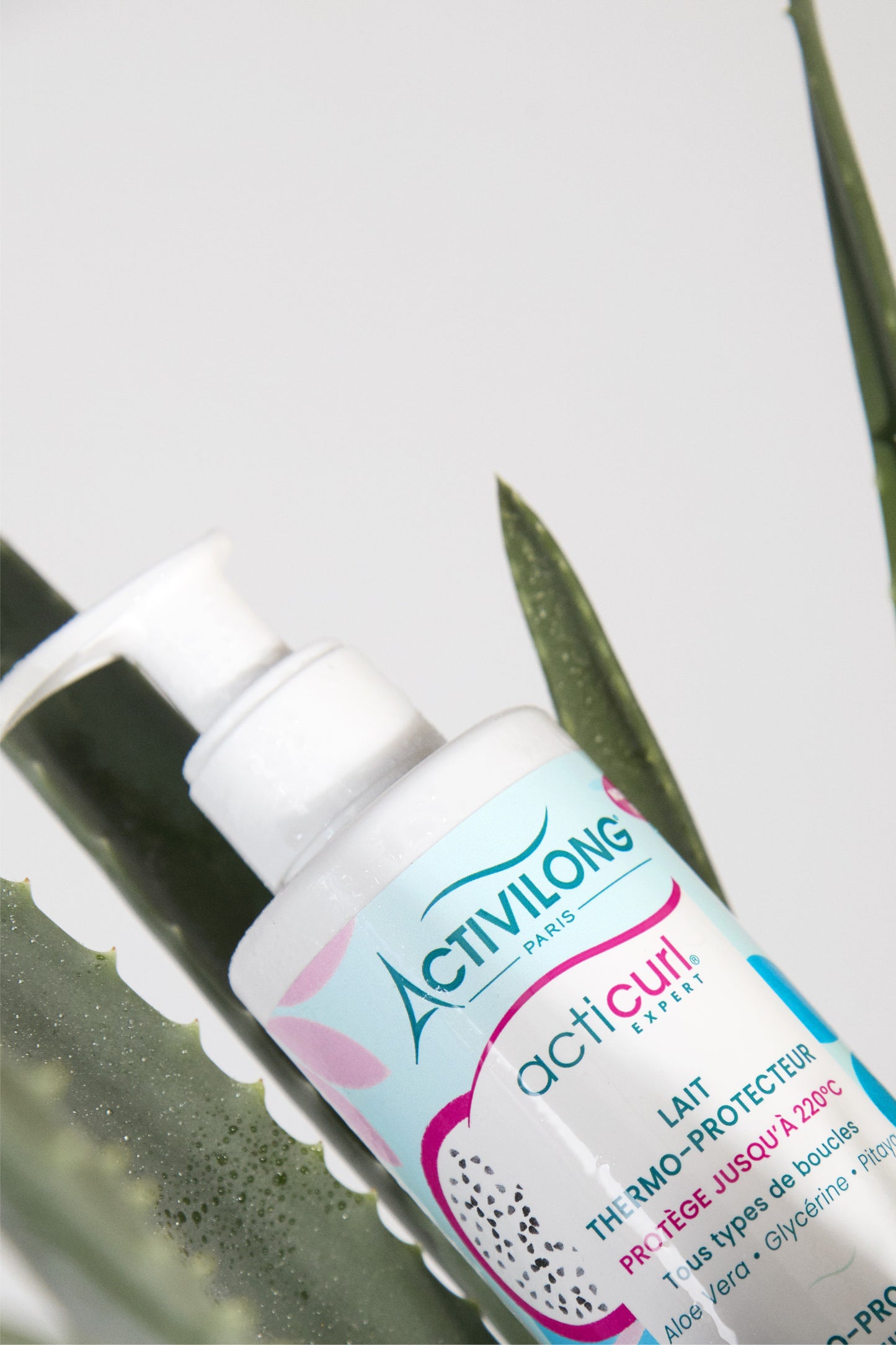 Flacon du lait thermo-protecteur Acticurl Expert posé sur des feuilles d’aloe vera