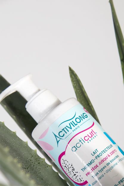Flacon du lait thermo-protecteur Acticurl Expert posé sur des feuilles d’aloe vera