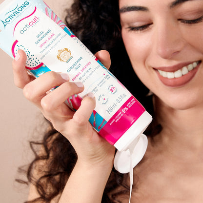 Femme souriante aux cheveux bouclés tenant la Gelée Scrunching Acticurl Expert
